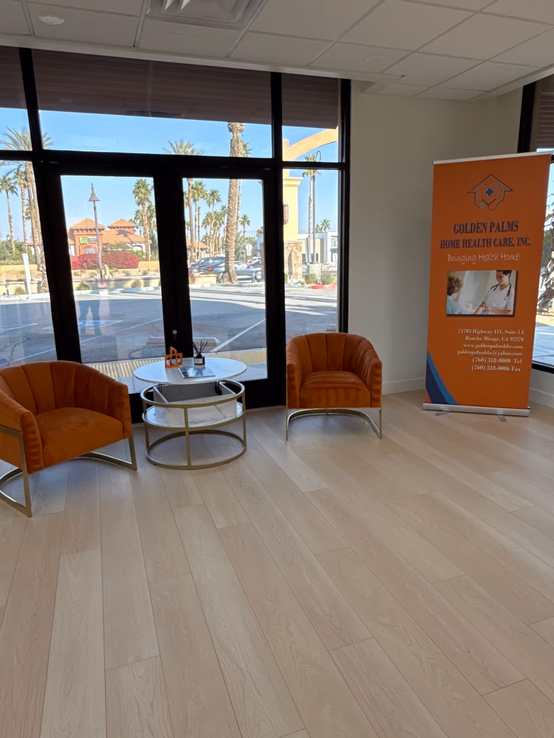 Interior waiting area with orange chairs, a glass coffee table, and a Golden Palms banner.