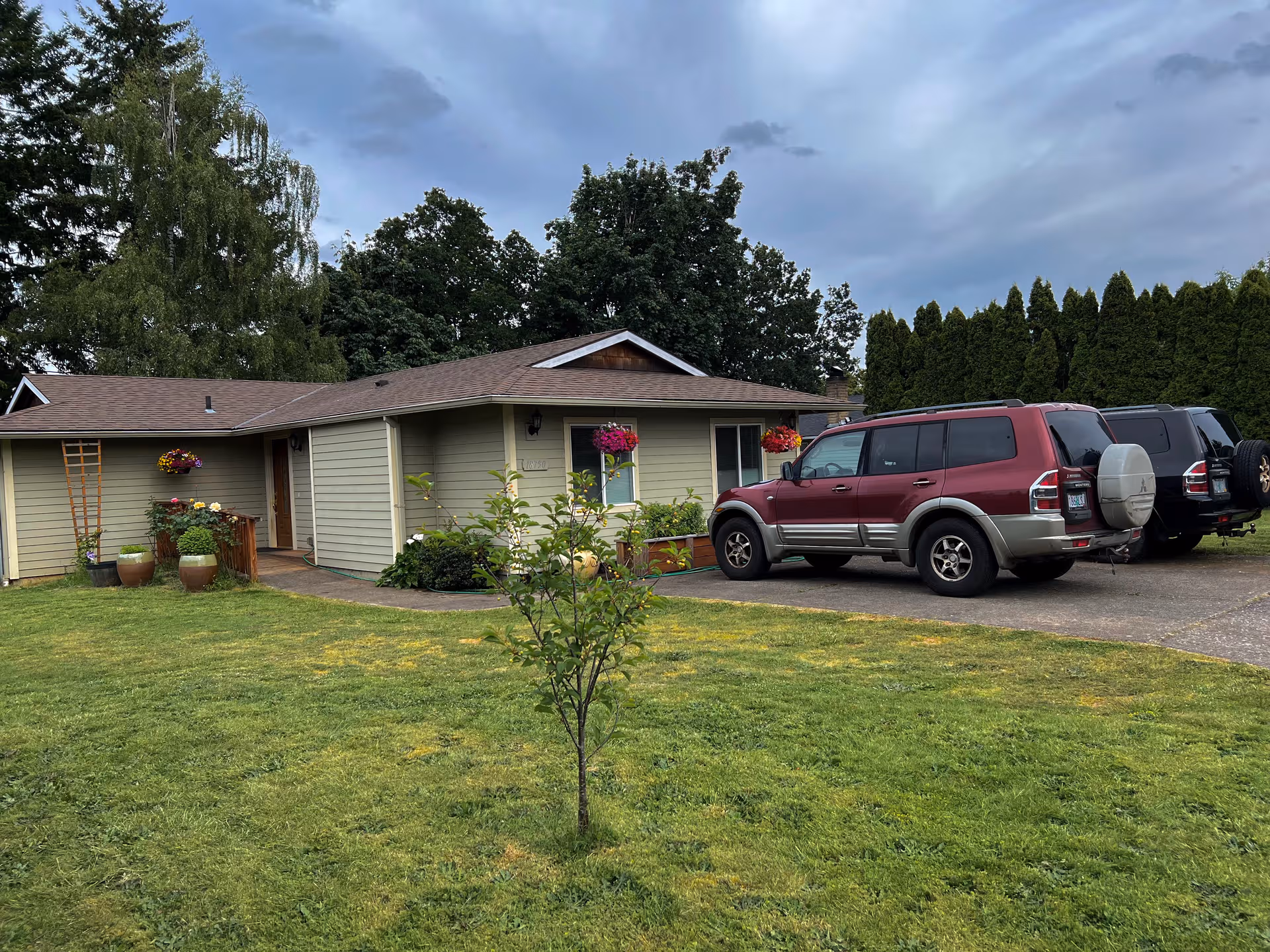 A single-story care home with beige siding, front yard, hanging baskets, and parked vehicles.