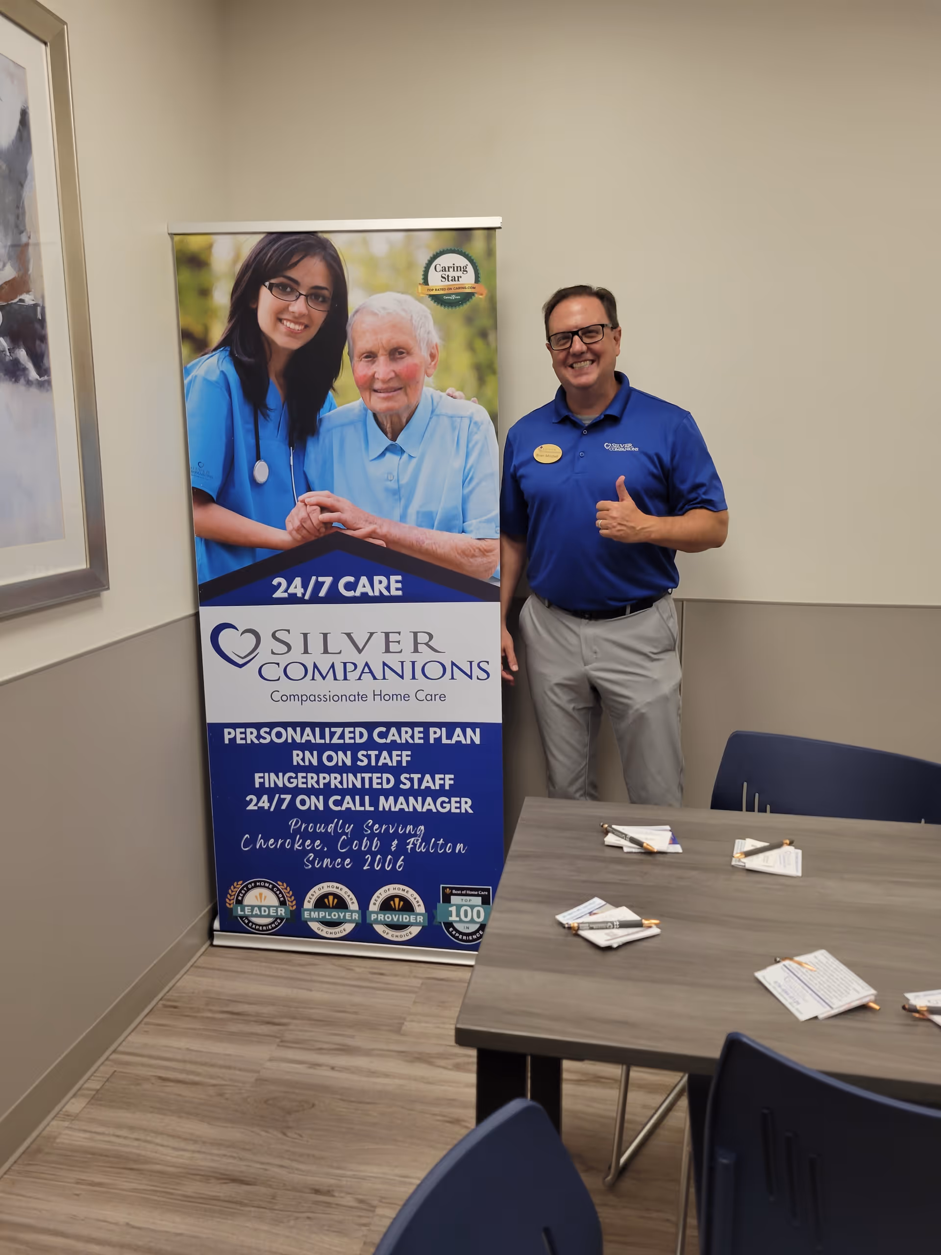 Man in blue polo stands beside a Silver Companions banner inside a meeting room.