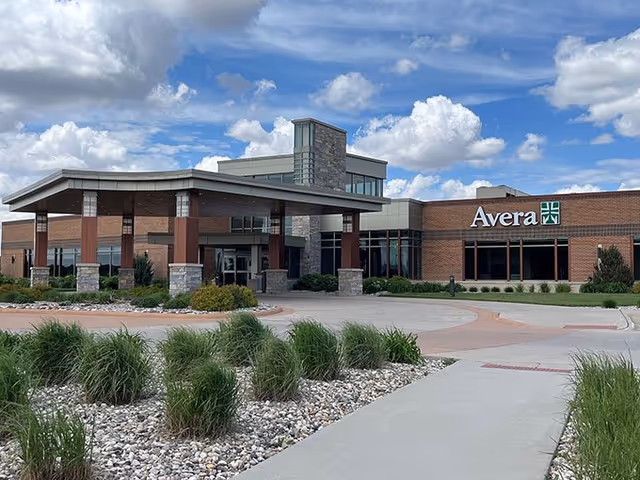 Exterior view of Avera building entrance with landscaping and blue sky.