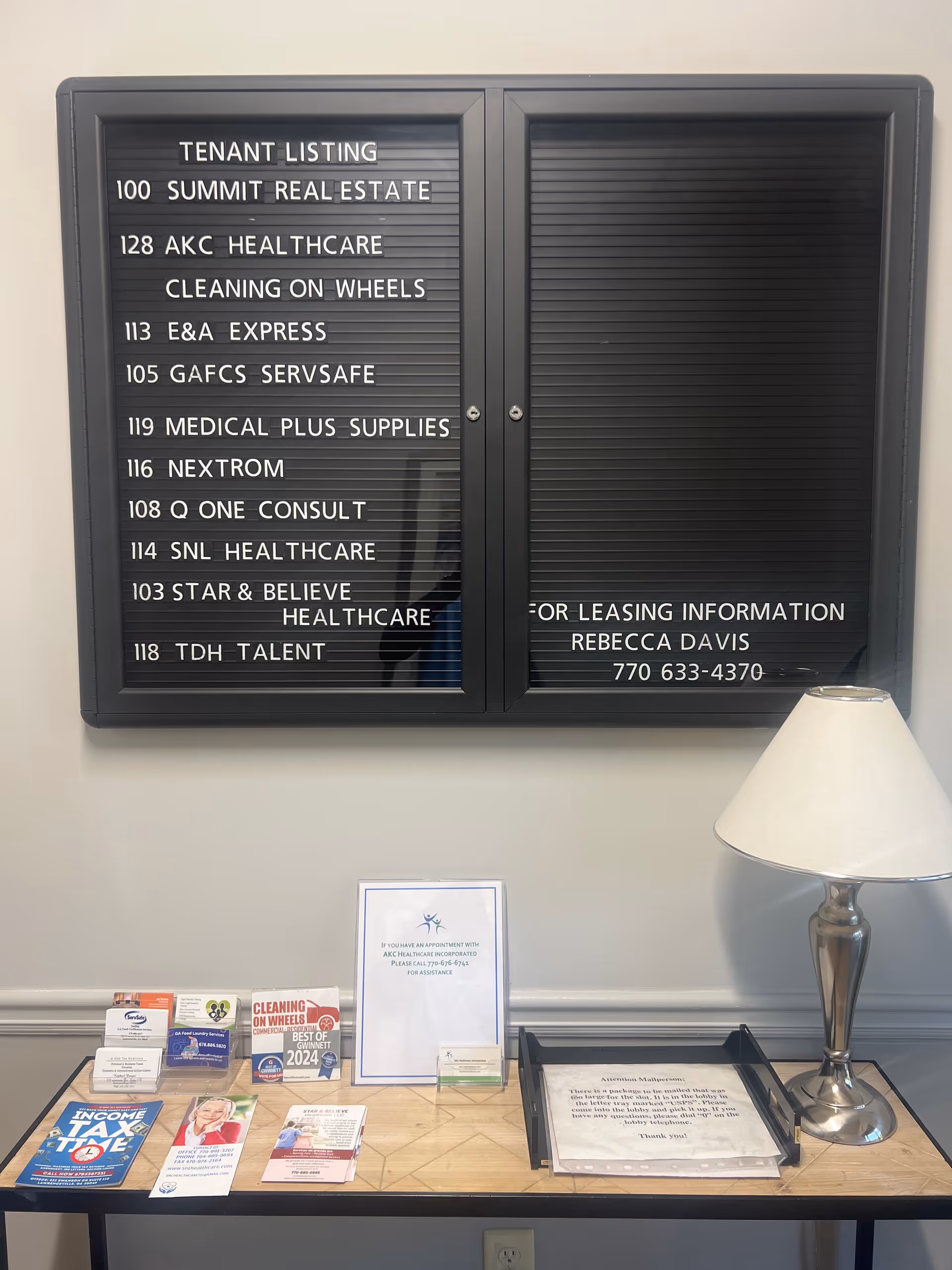 Interior lobby with tenant listing board, brochures, and a table lamp.