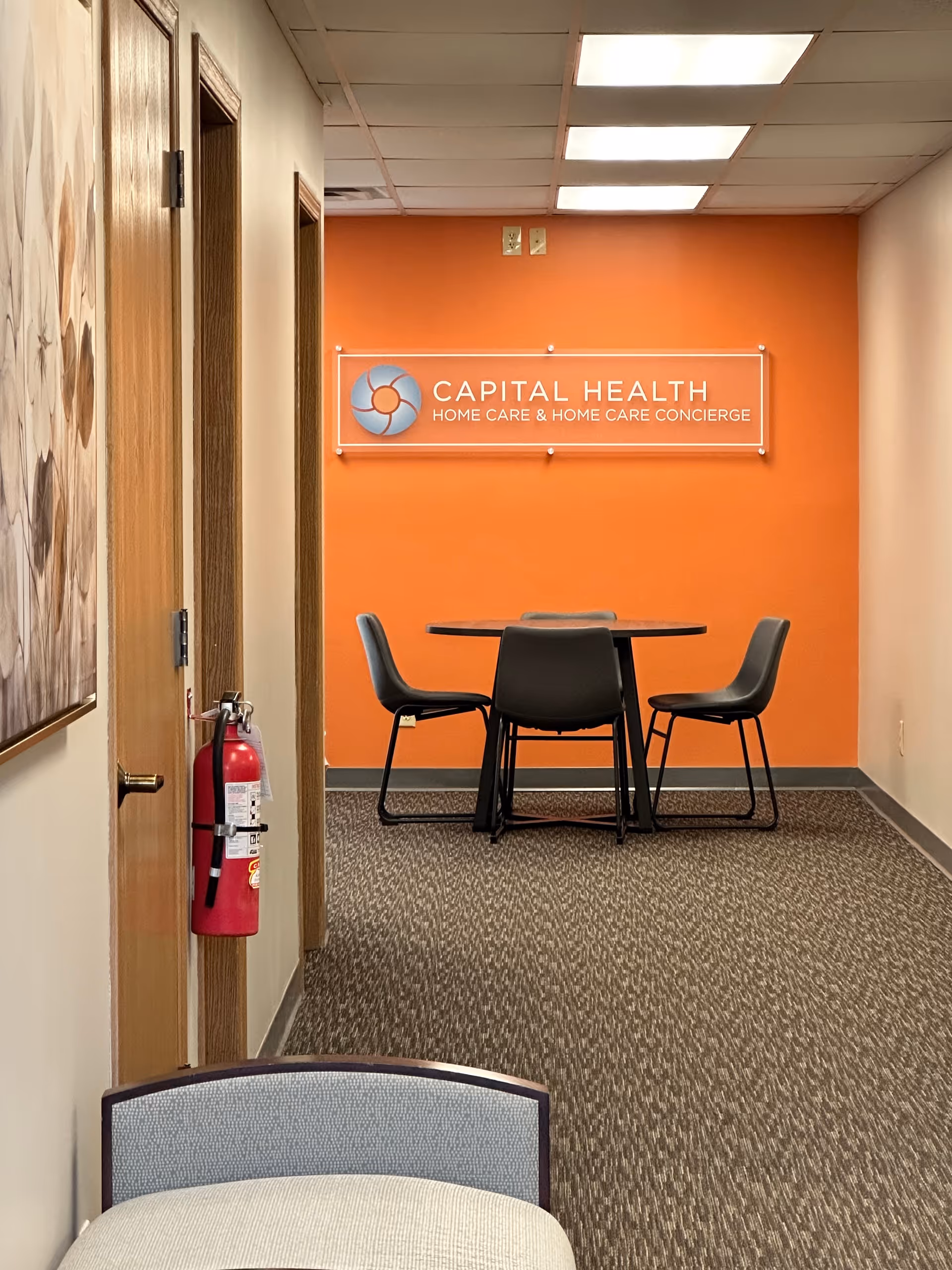 Interior hallway with orange wall, Capital Health sign, and a round table with four chairs.