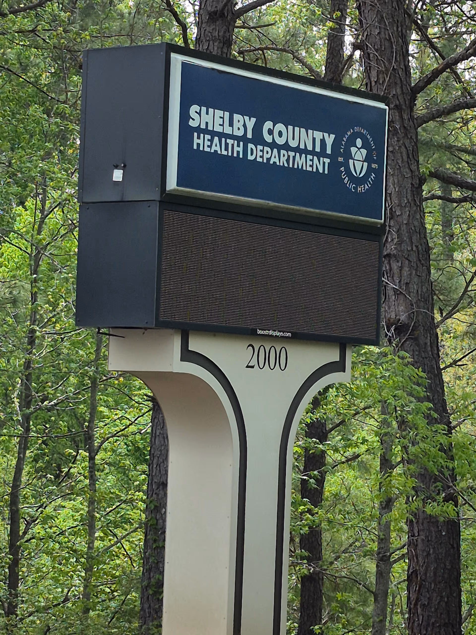 Shelby County Health Department sign on a pedestal amid trees in a wooded area.
