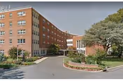 Brick senior living facility with curved wings and a driveway in front.