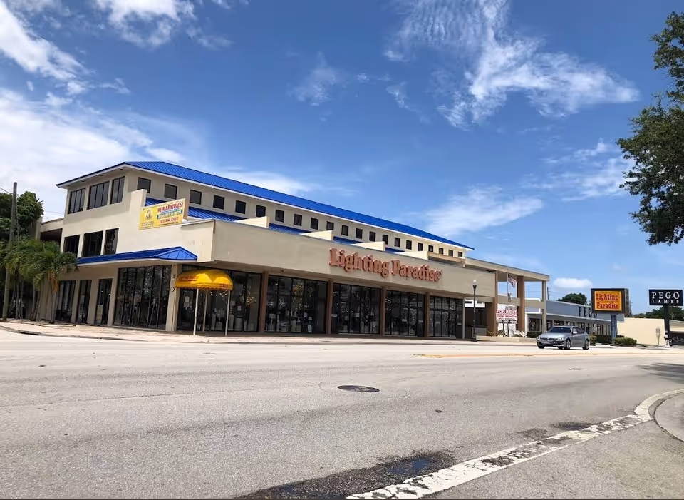 Two-story commercial building with glass storefronts and a bright blue roof on a sunny day.