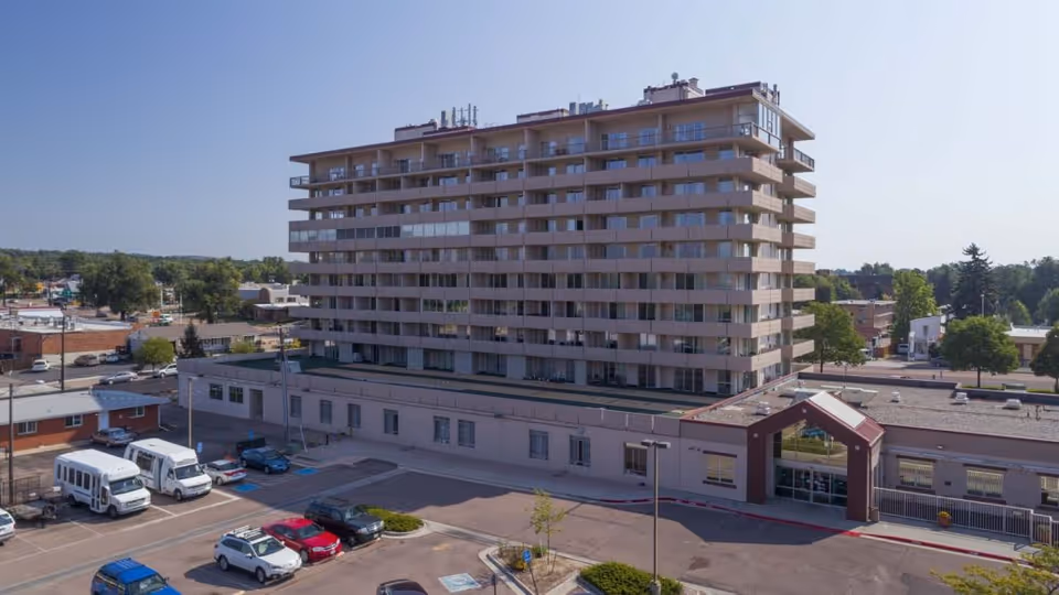 Exterior view of a multi-story building with balconies, part of Medallion Post Acute Rehabilitation facility, surrounded by a parking lot with several cars and vans, under a clear blue sky.