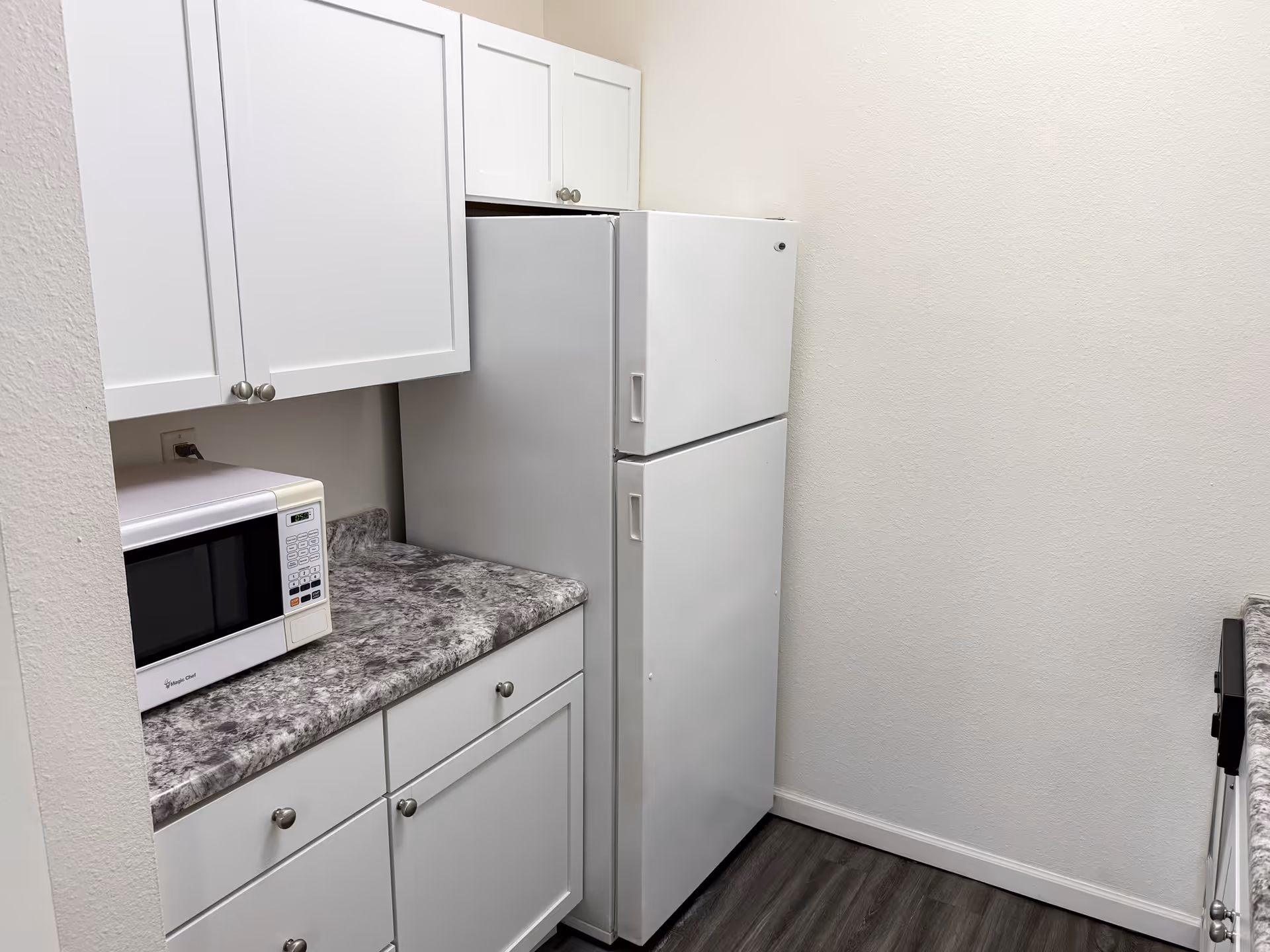 White kitchen cabinets, microwave, and a refrigerator against a marble-patterned countertop.