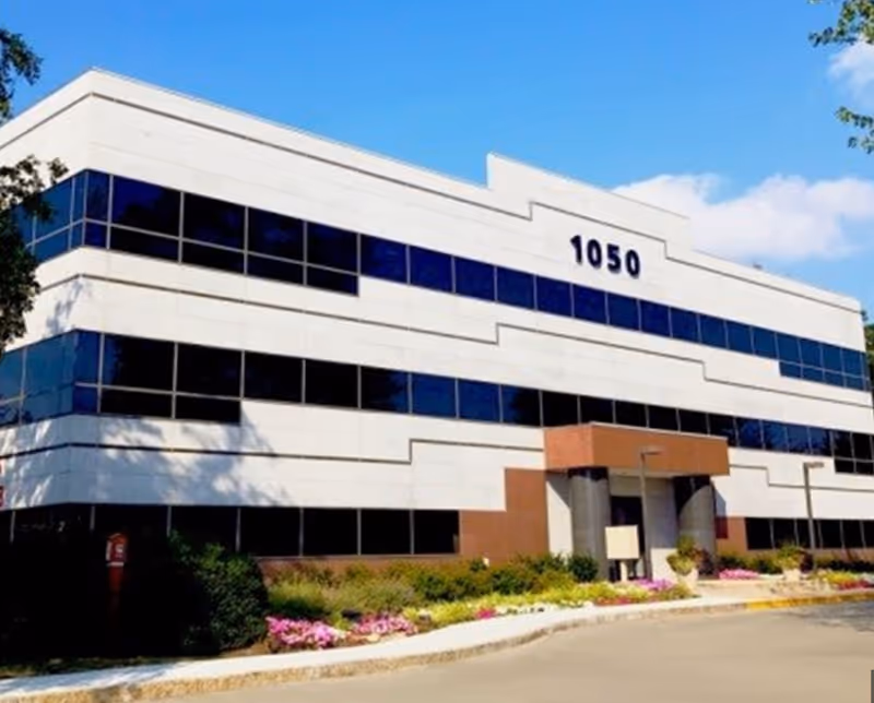 White, modern senior living building with blue-tinted windows address 1050