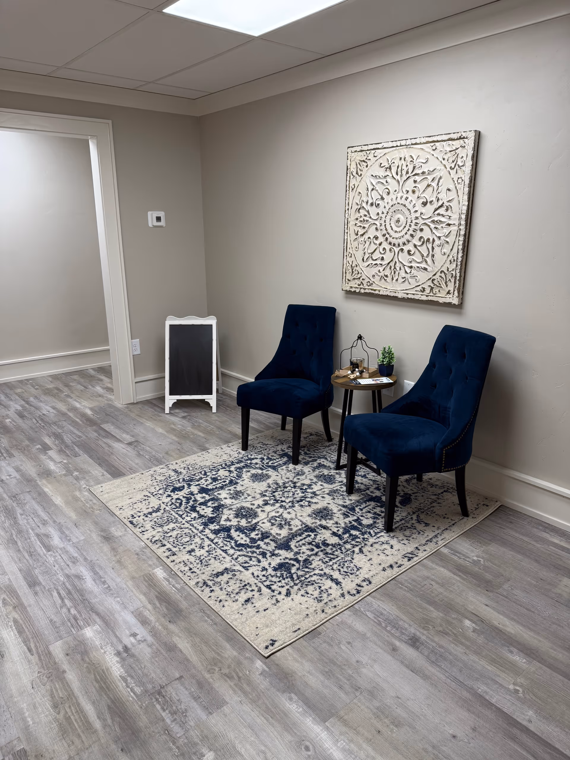 Two navy chairs and a small table sit on a patterned rug in a neutral lobby.
