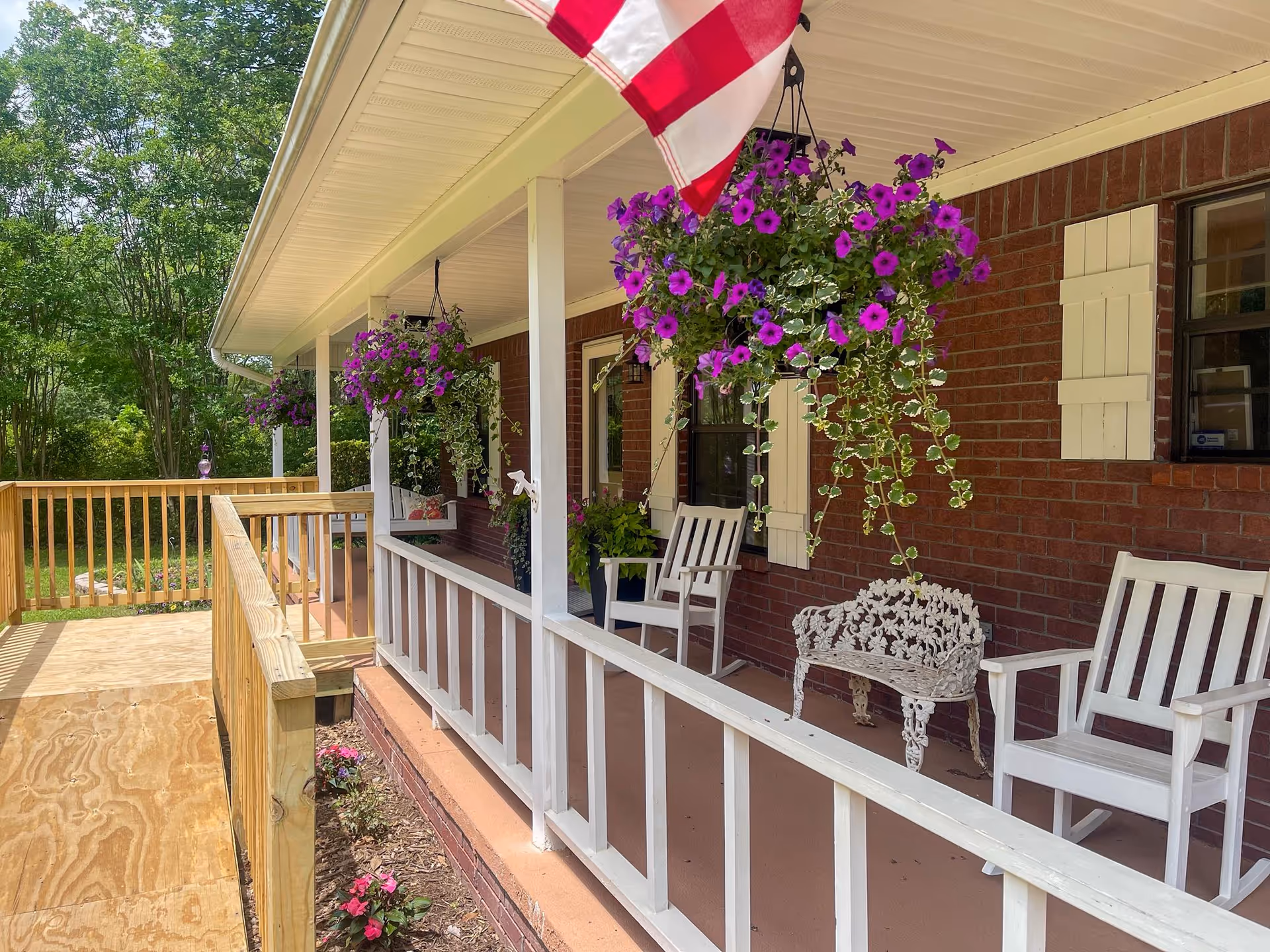 Front porch of Golden Oaks Care Home with hanging purple flowers and white chairs.