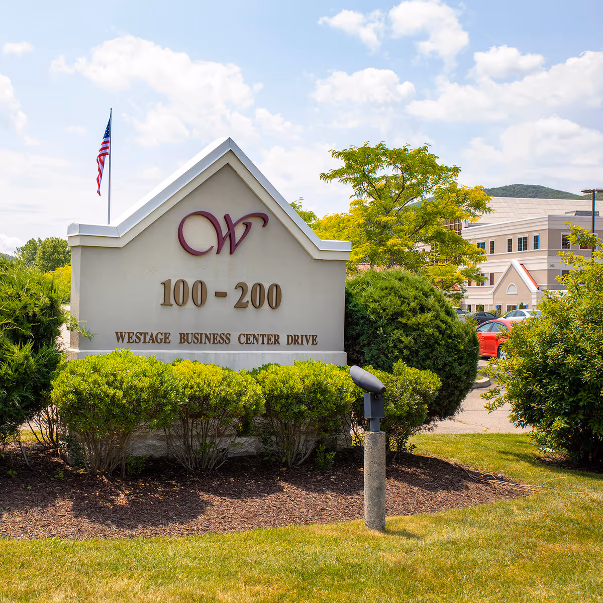 Outdoor view of a facility sign with bushes and a building in the background.