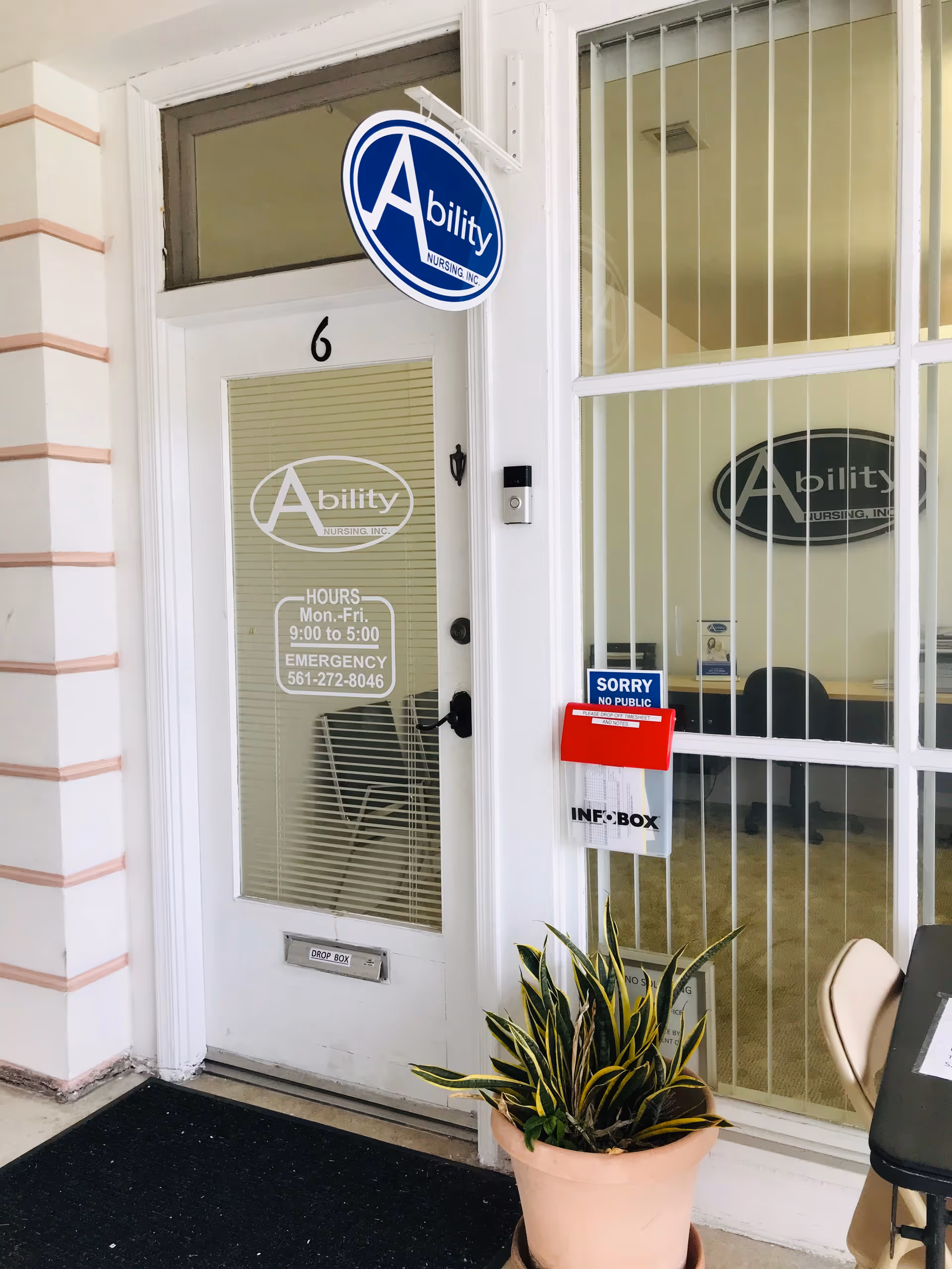 Exterior entrance of Ability Nursing Inc with blue circular sign, glass door, and potted plant.