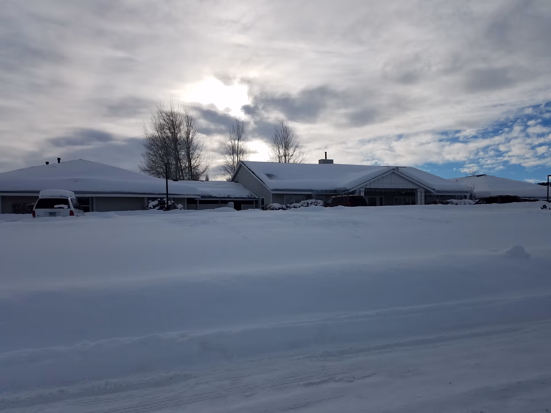 Snow-covered, single-story senior living center with parked cars and a cloudy sky.