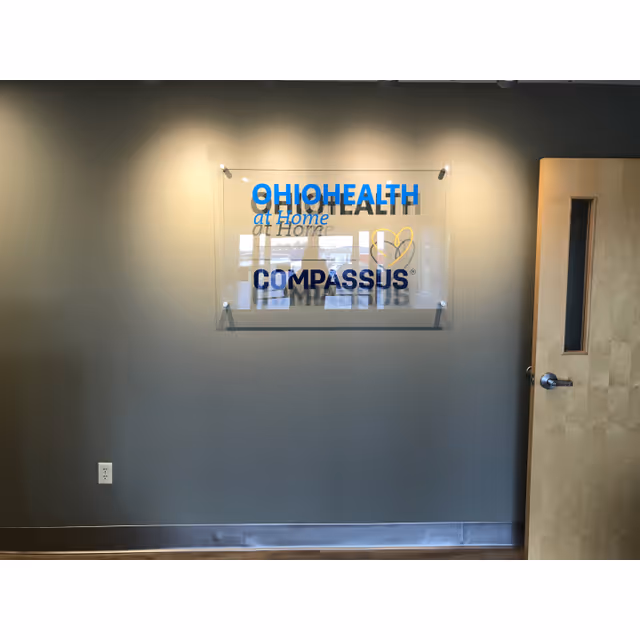 Interior wall with a glass plaque displaying OhioHealth at Home Compassus, next to a wooden door.