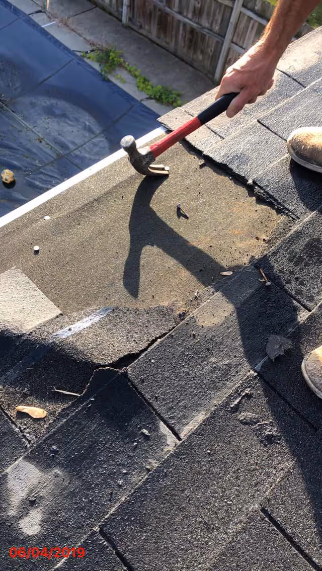 A person hammering roof shingles outdoors during maintenance.