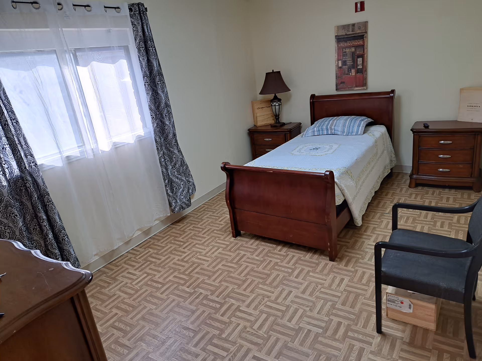 A bedroom with a wooden bed, two nightstands, dressers, a lamp, and a window with curtains.