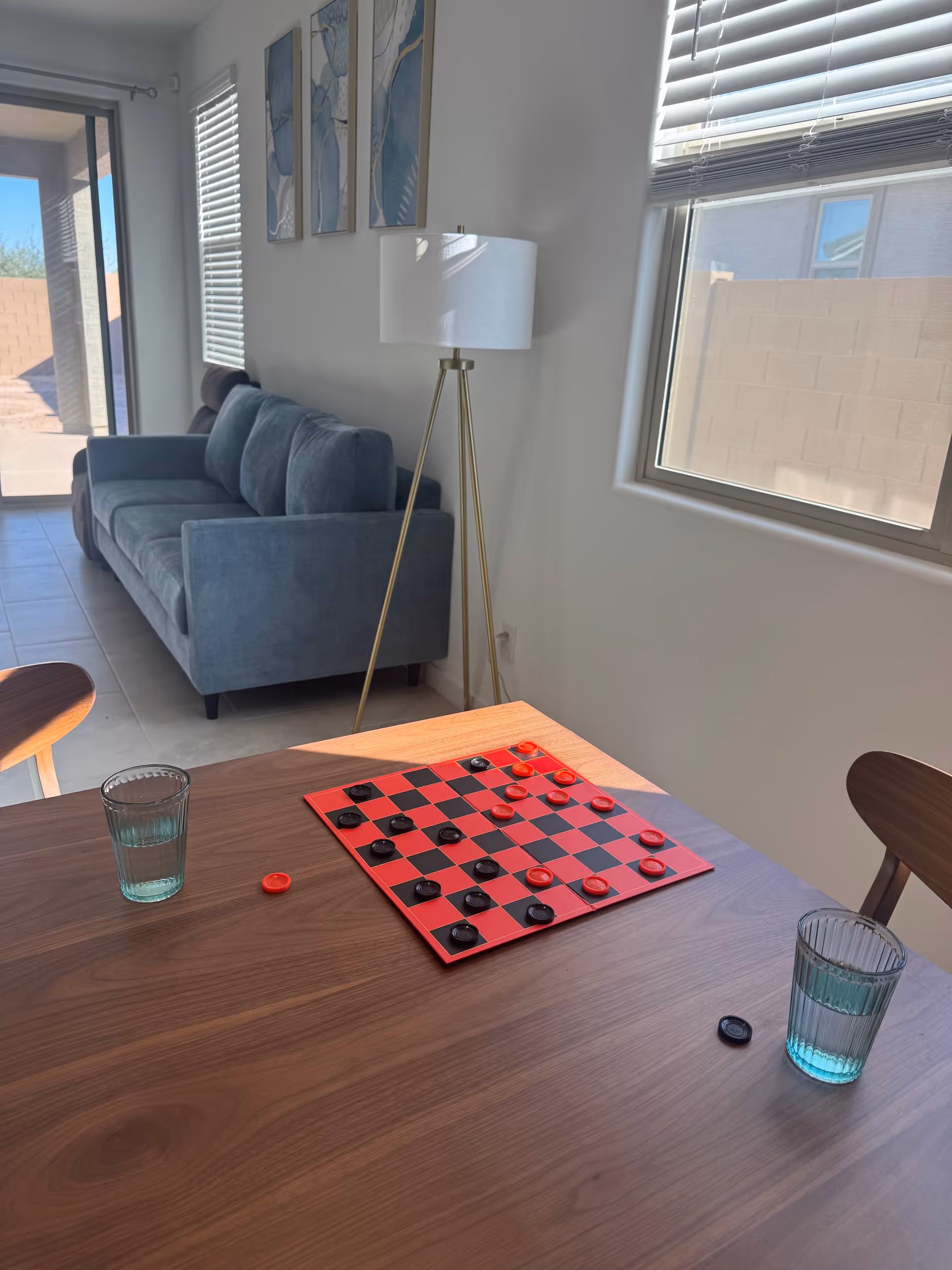 Bright living room with blue sofa, floor lamp, windows, and a checkers board on the table.