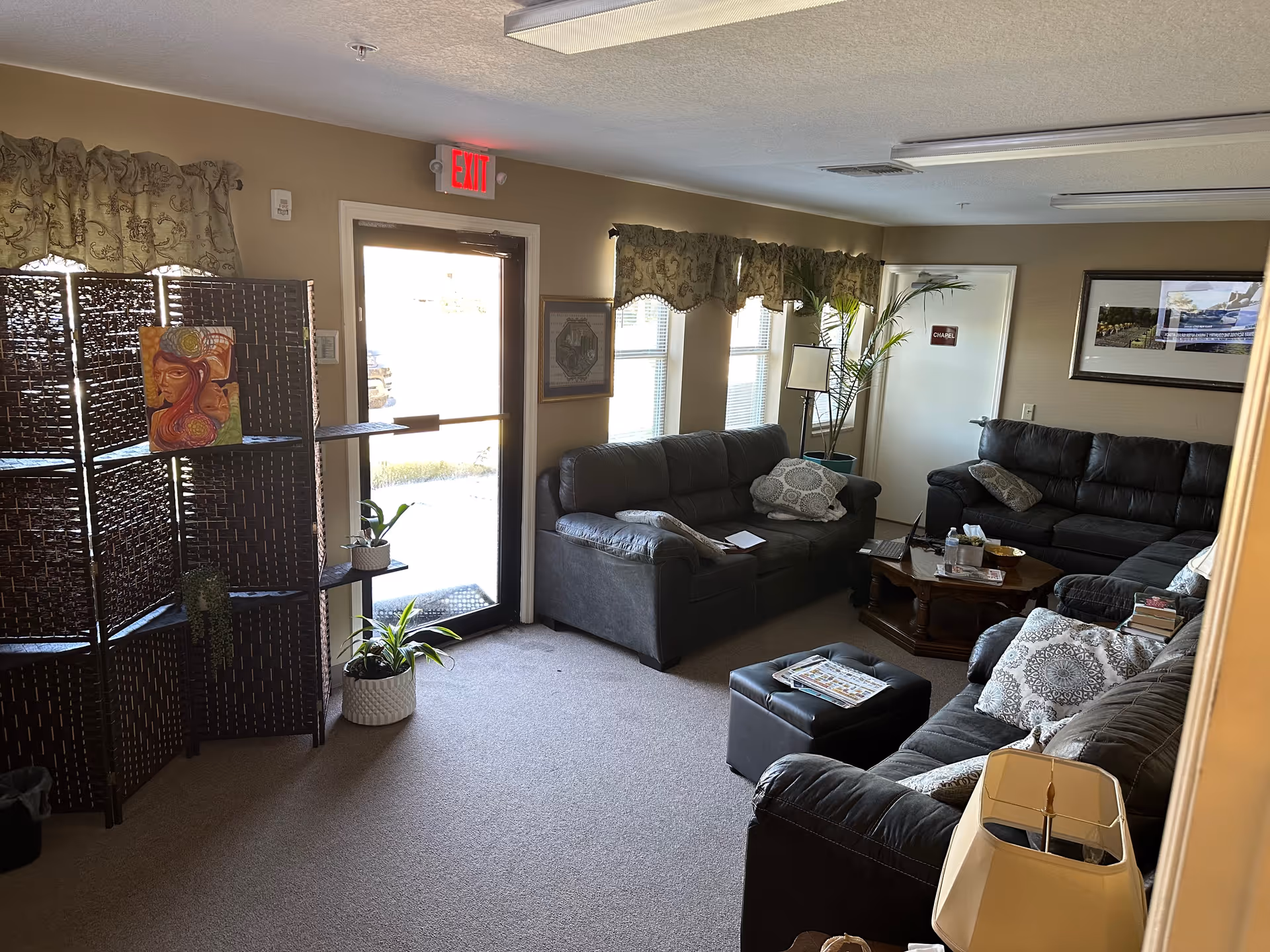 Cozy living room with dark leather sofas, plants, and an exit door.
