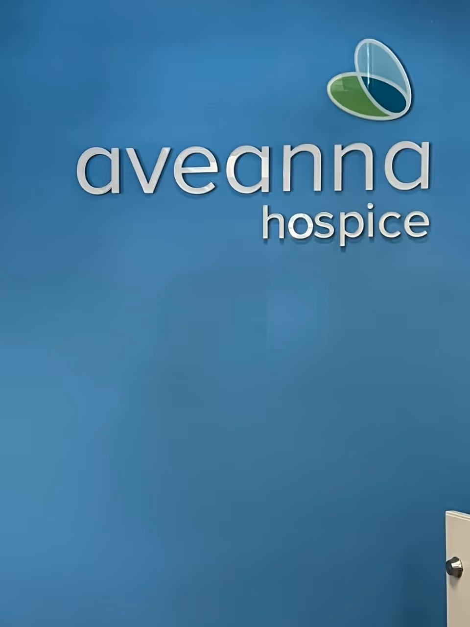 Blue interior wall with Aveanna Hospice sign and door handle.