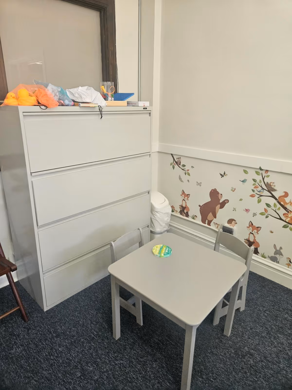 Child-sized table and chairs beside a white dresser in a mural-covered interior.