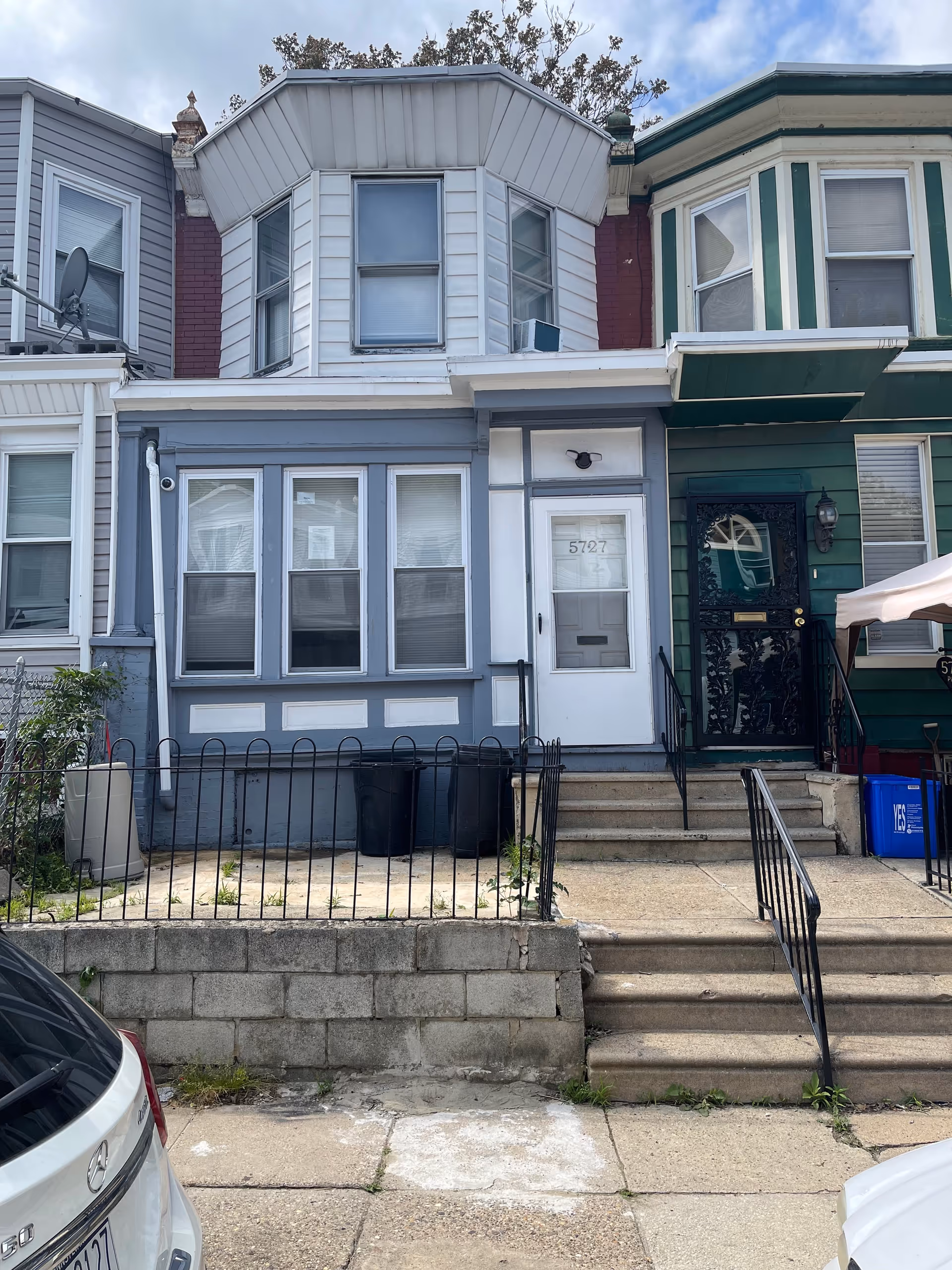 Row house exterior with blue facade, steps to the door, and bay windows.