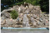 Outdoor rock waterfall feature with flowing water in a sunny courtyard.