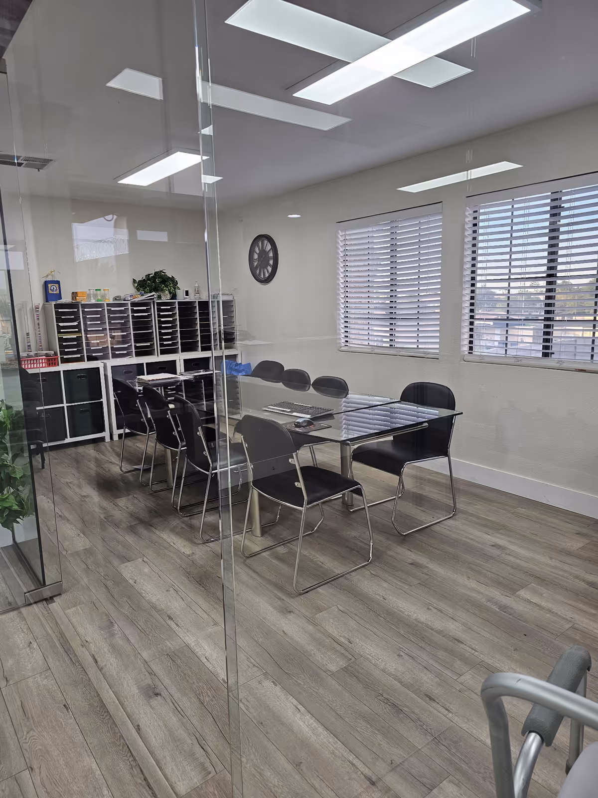 Glass-walled conference room with black chairs around a glass table and mail shelving.