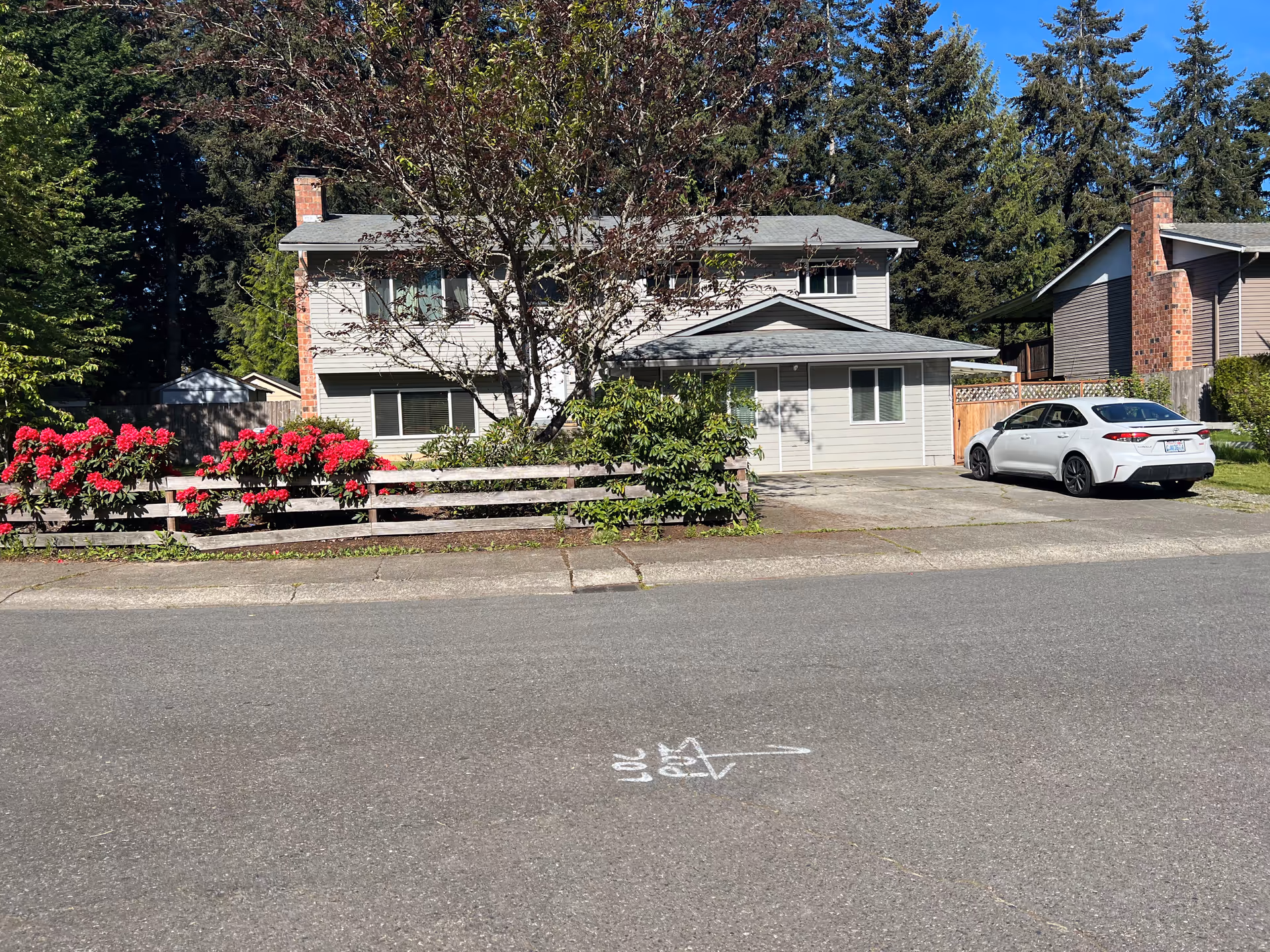 Exterior of a two-story senior living home with a driveway, white car, and flowering bushes.