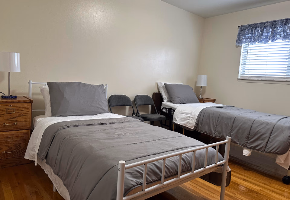 Two twin beds with gray bedding and nightstands in a simple, quiet bedroom.