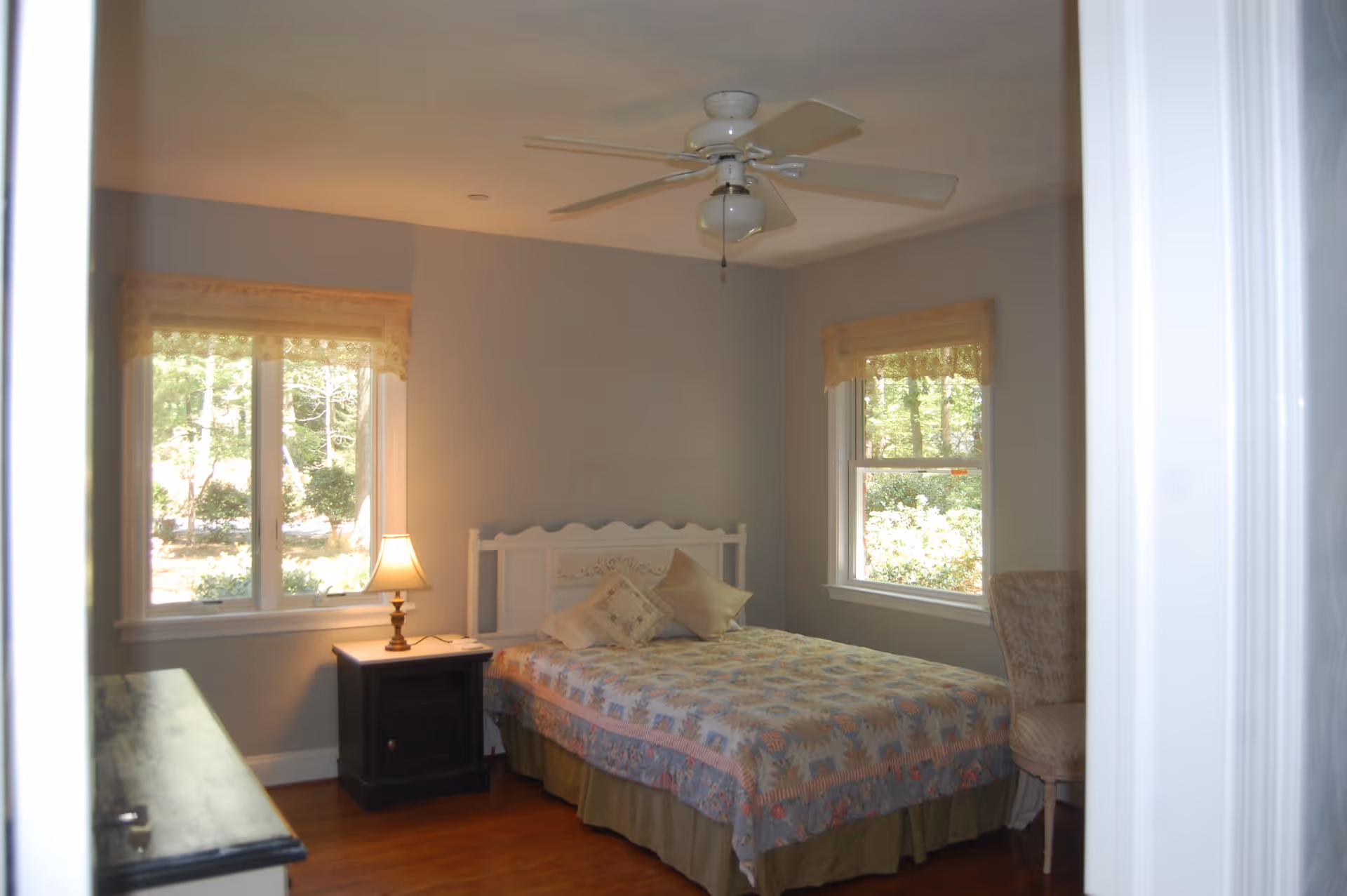 Cozy bedroom with a bed, nightstand, lamp, windows, and a ceiling fan.