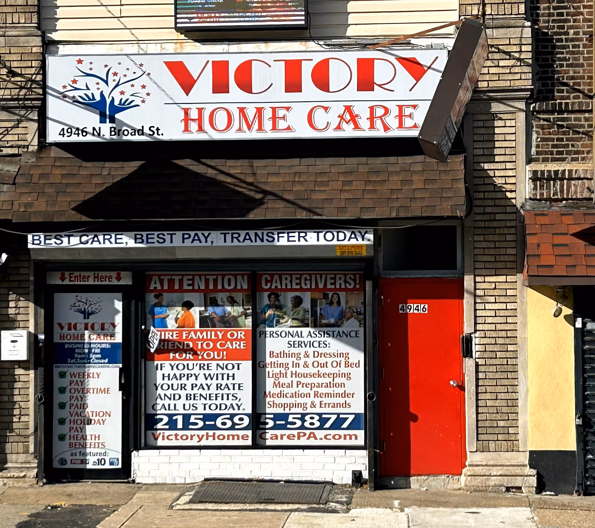 Storefront of Victory Home Care with large sign, red door, and window posters.