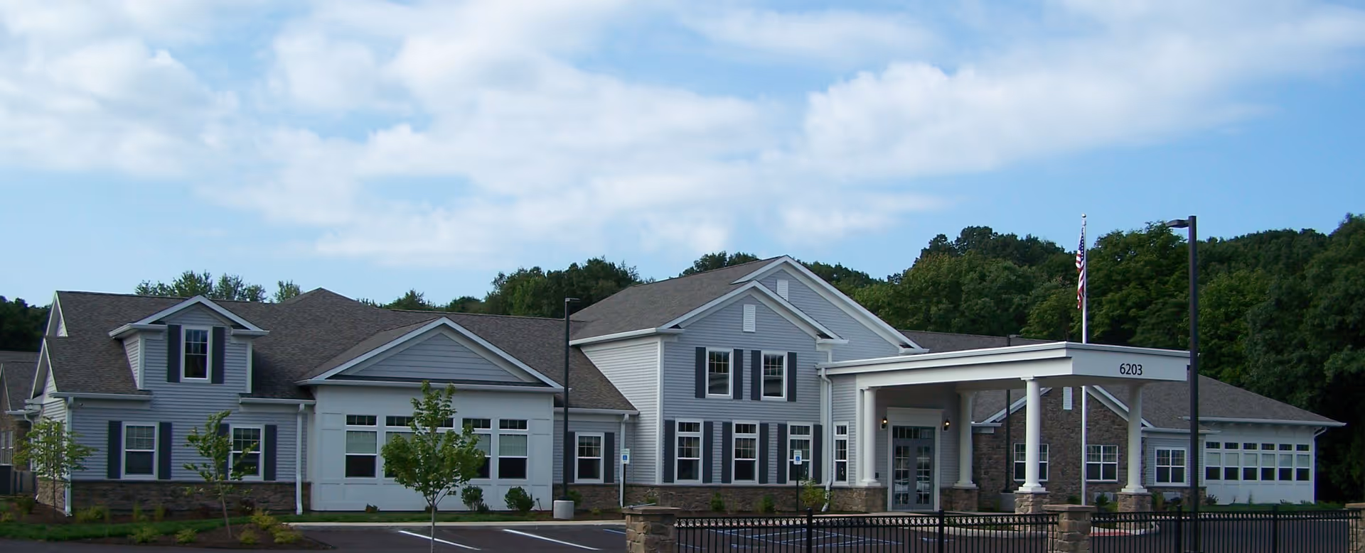 Modern senior living facility with a gray multi-wing building and a covered front entrance.