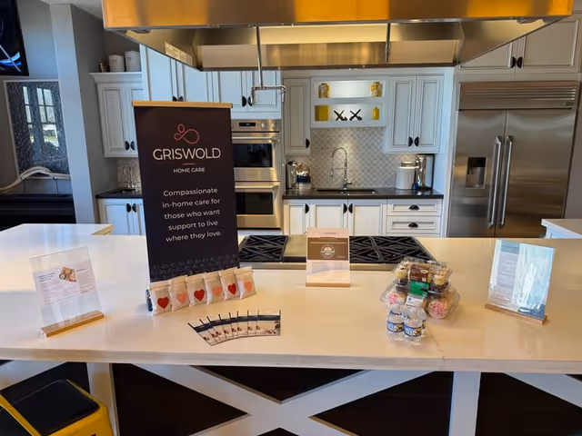 Modern white kitchen with island counter, brochures, and a Griswold Home Care sign.