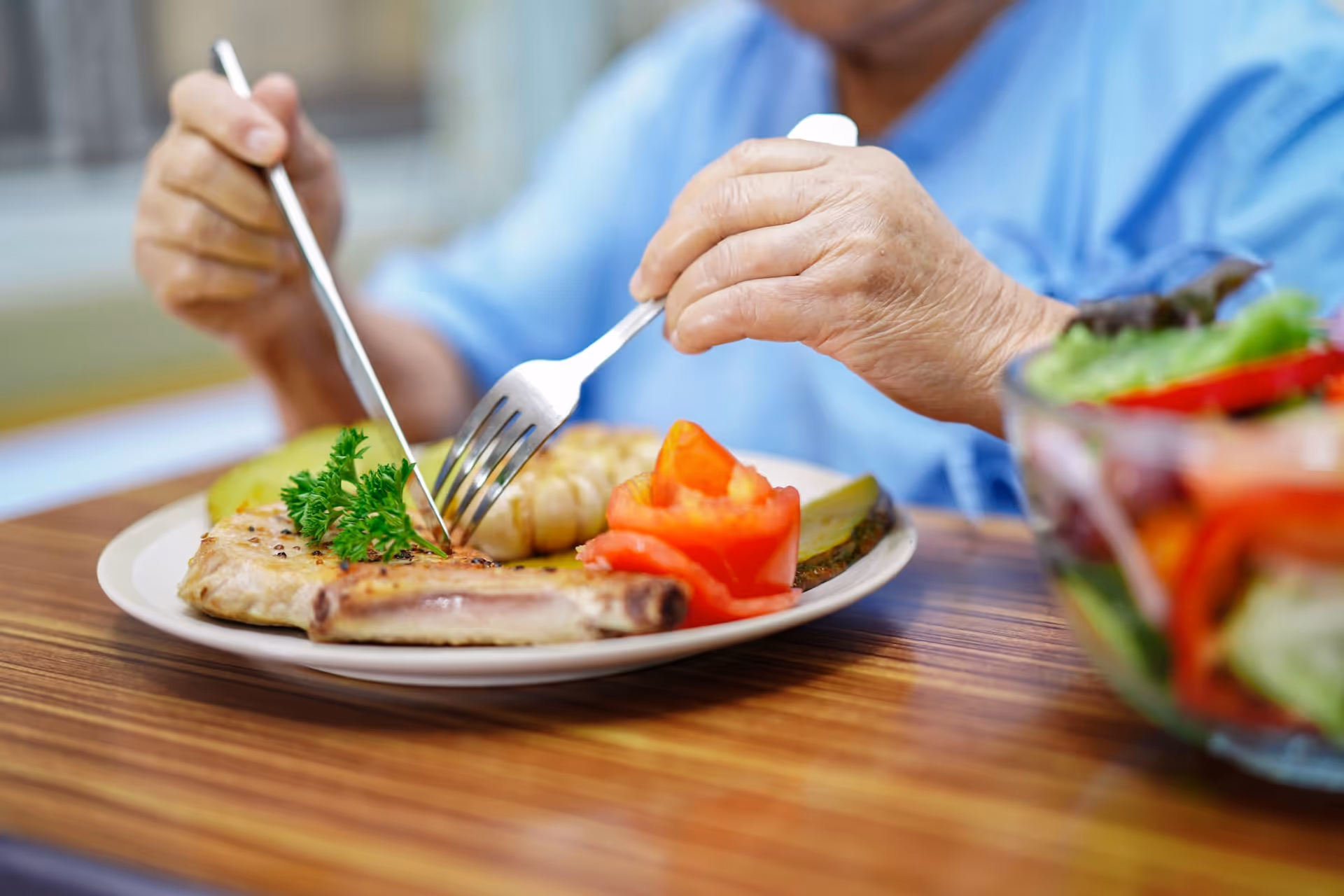 A person in blue cuts a plated meal at a wooden table.