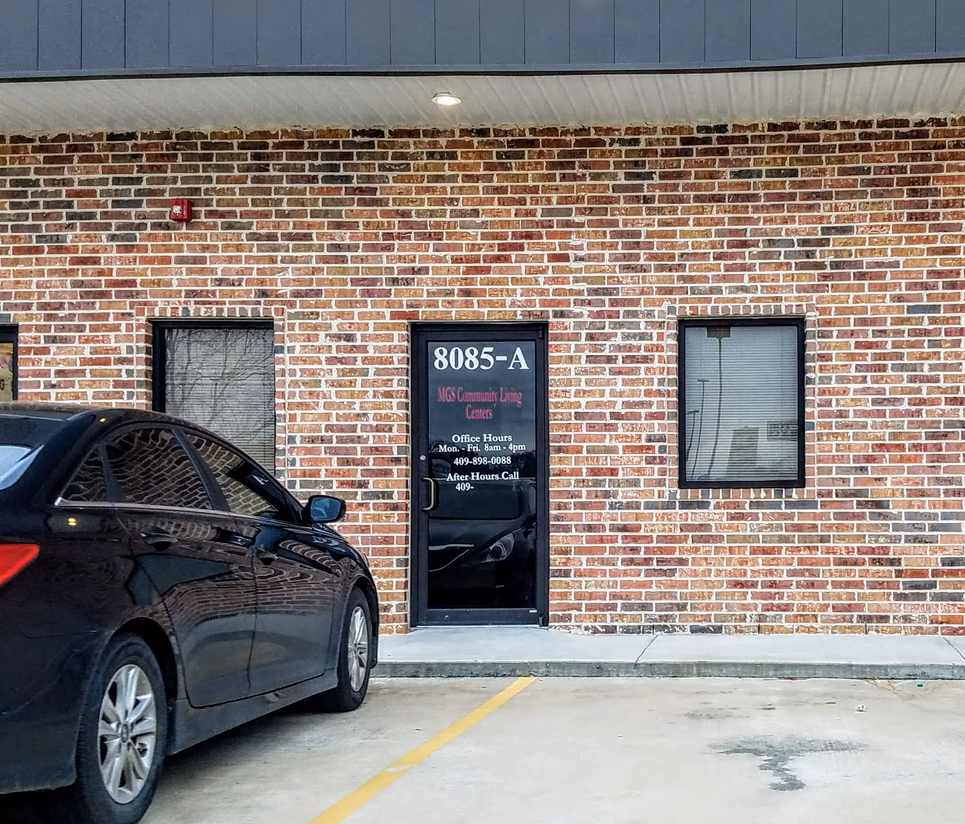 Brick exterior wall with a door labeled 8085-A and a parked car in foreground