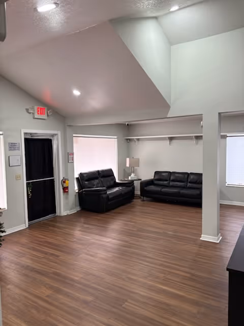 A spacious living area with black leather sofas, wood floors, and an exit door.