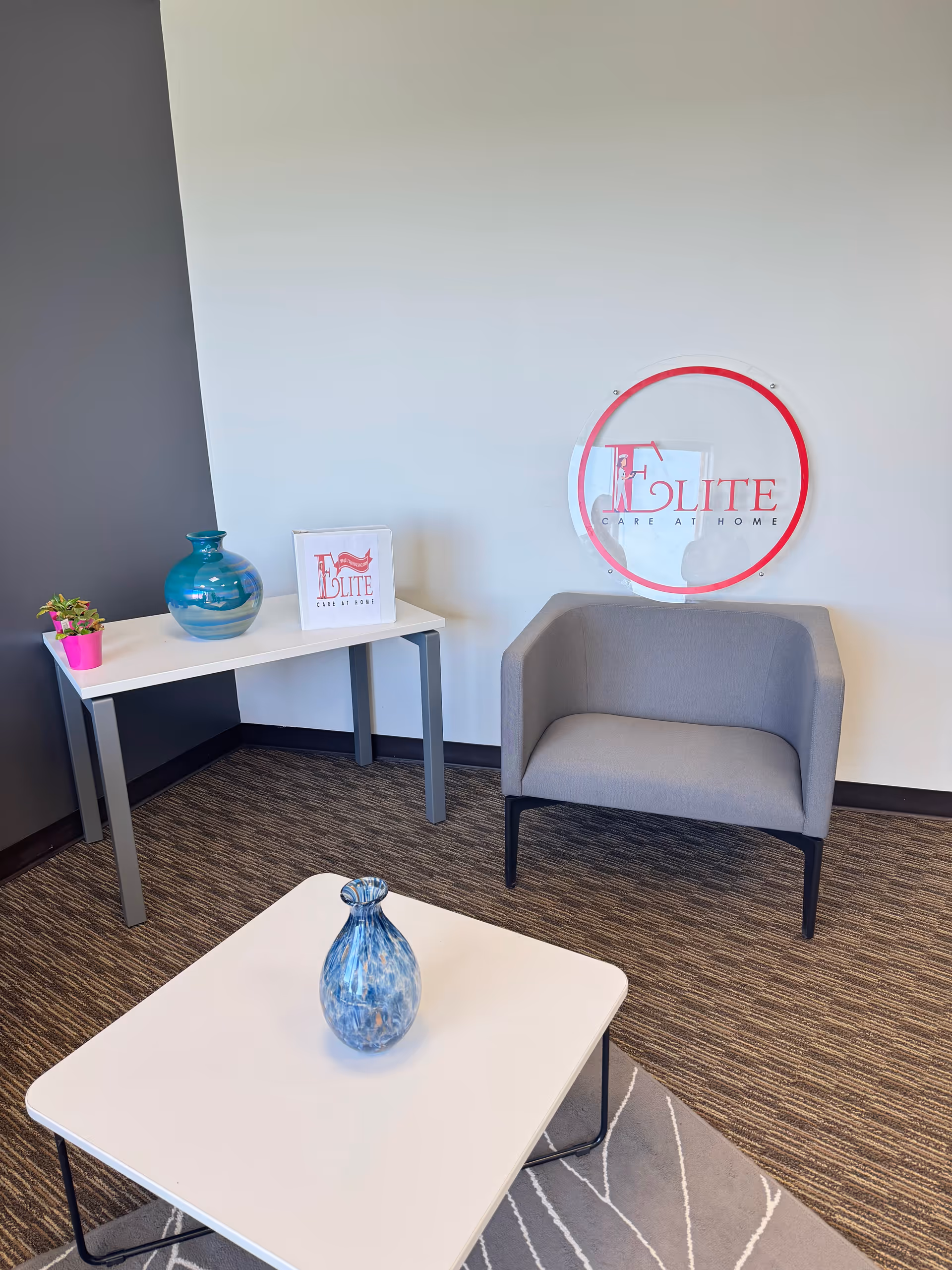 Modern lobby seating area featuring a chair, coffee table, vases, and Elite Care sign.