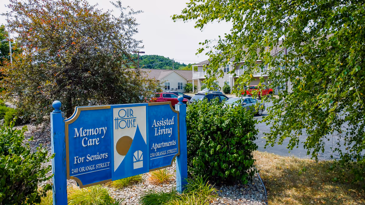 Blue sign advertising memory care and assisted living in front of a senior living facility.