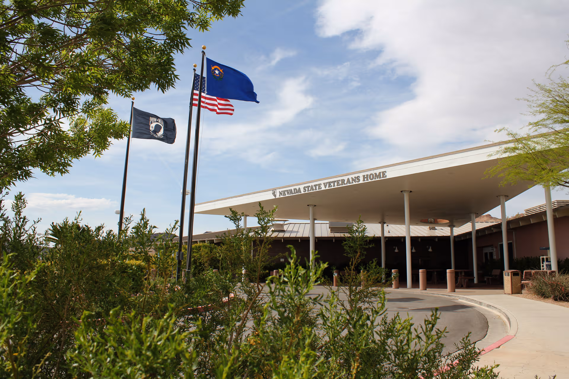 Front view of Nevada State Veterans Home with flags, canopy, and landscaped entrance.