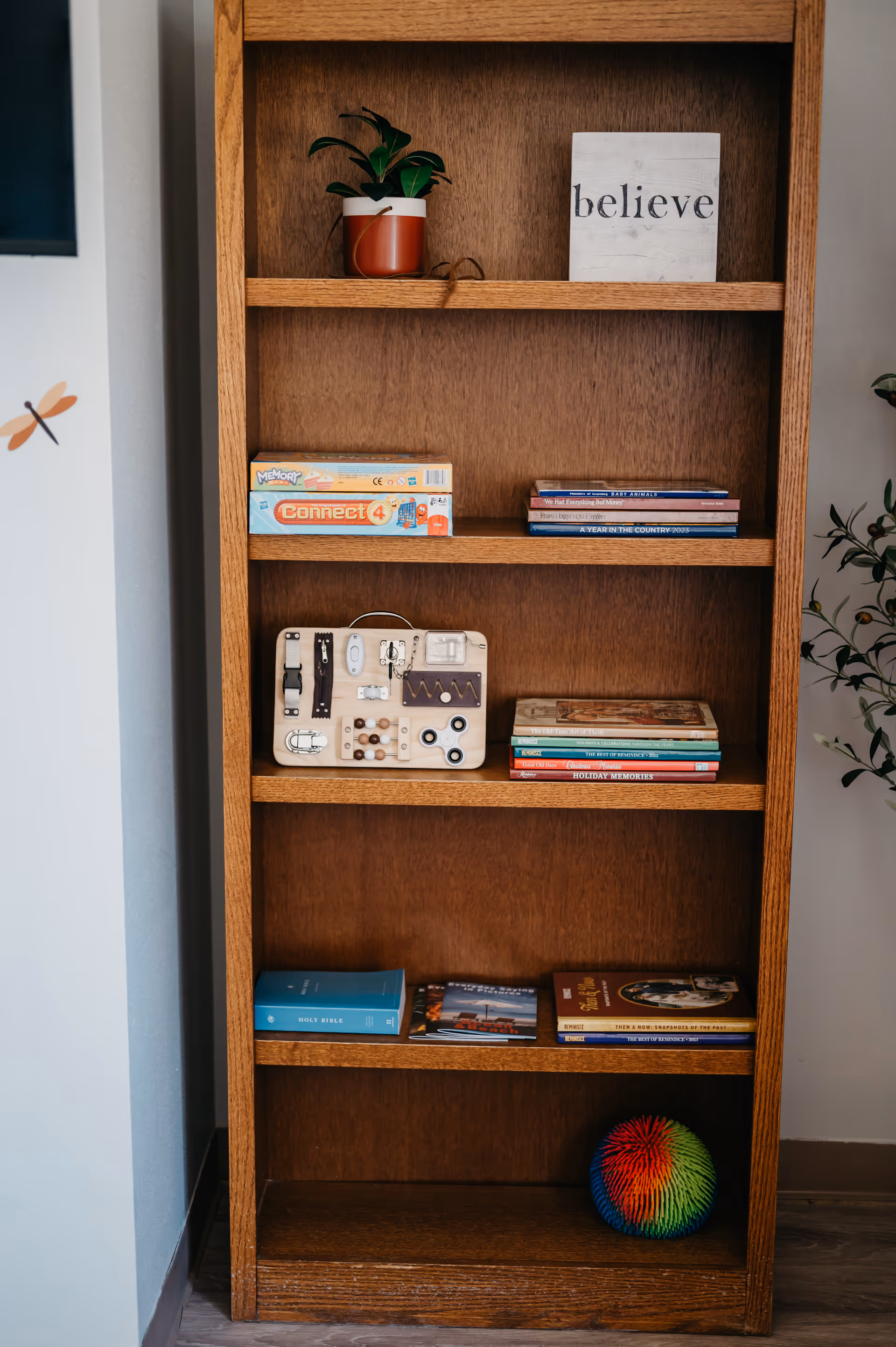 Wooden bookshelf in a cozy interior with plants, books, and a 'believe' sign.