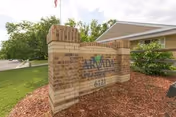Brick entry sign reading Arvada Care and Rehabilitation Center with landscaped lawn and driveway.