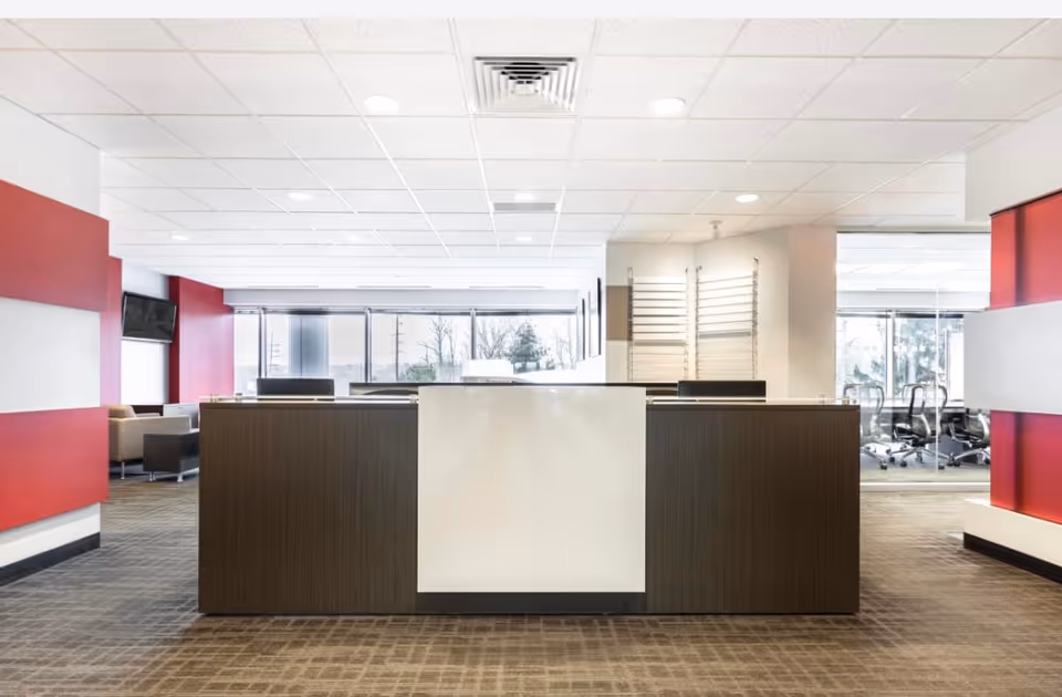 Modern lobby featuring a dark reception desk, red accents, and a seating area in the background.