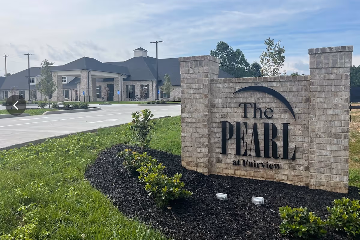 Exterior view of The Pearl at Fairview senior living facility with brick sign and entrance.