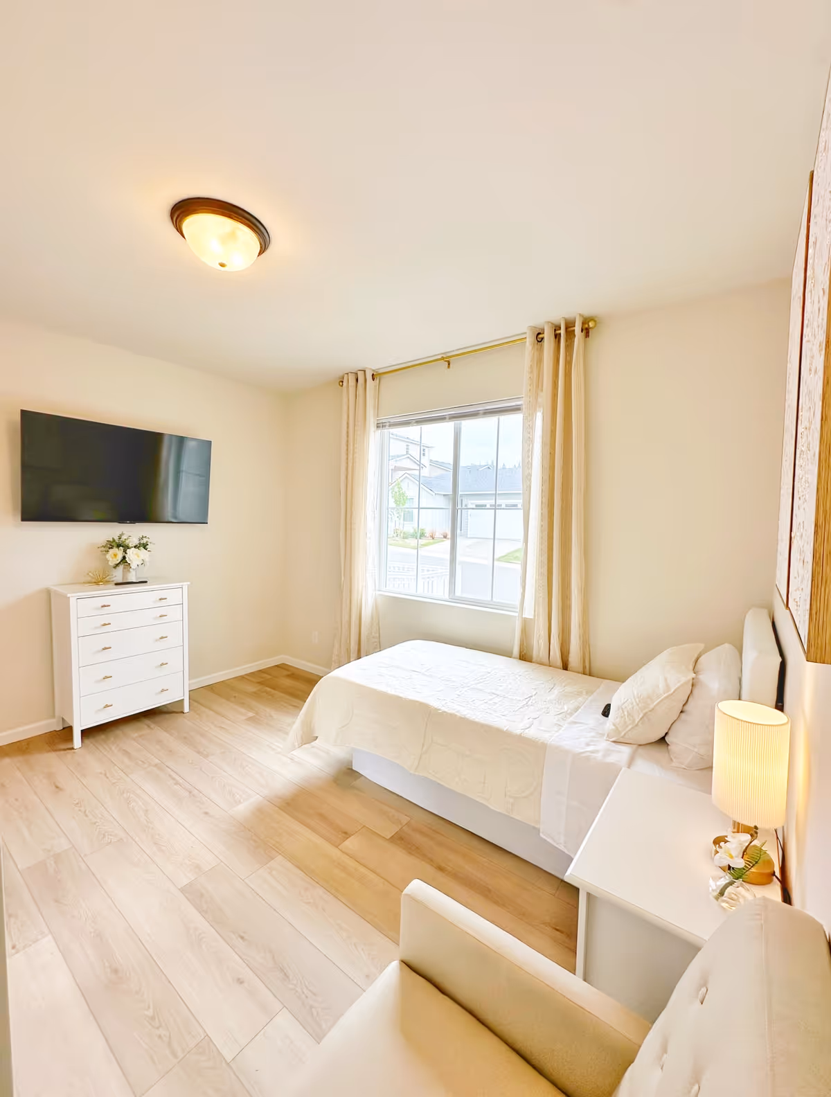 Bright, uncluttered bedroom with a single bed, dresser, TV, and a window with curtains.