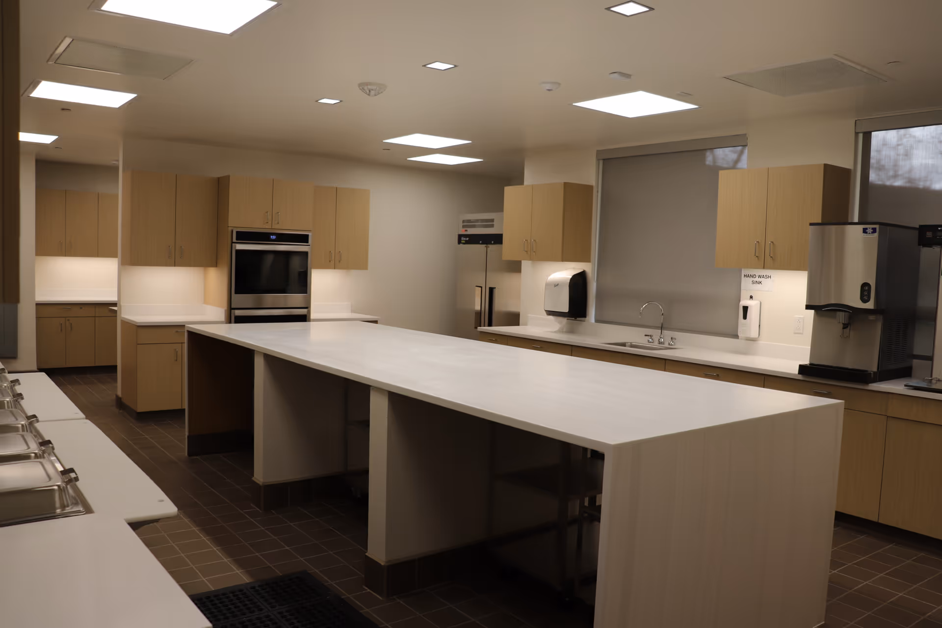 Bright institutional kitchen featuring a central island, cabinets, and built-in appliances.