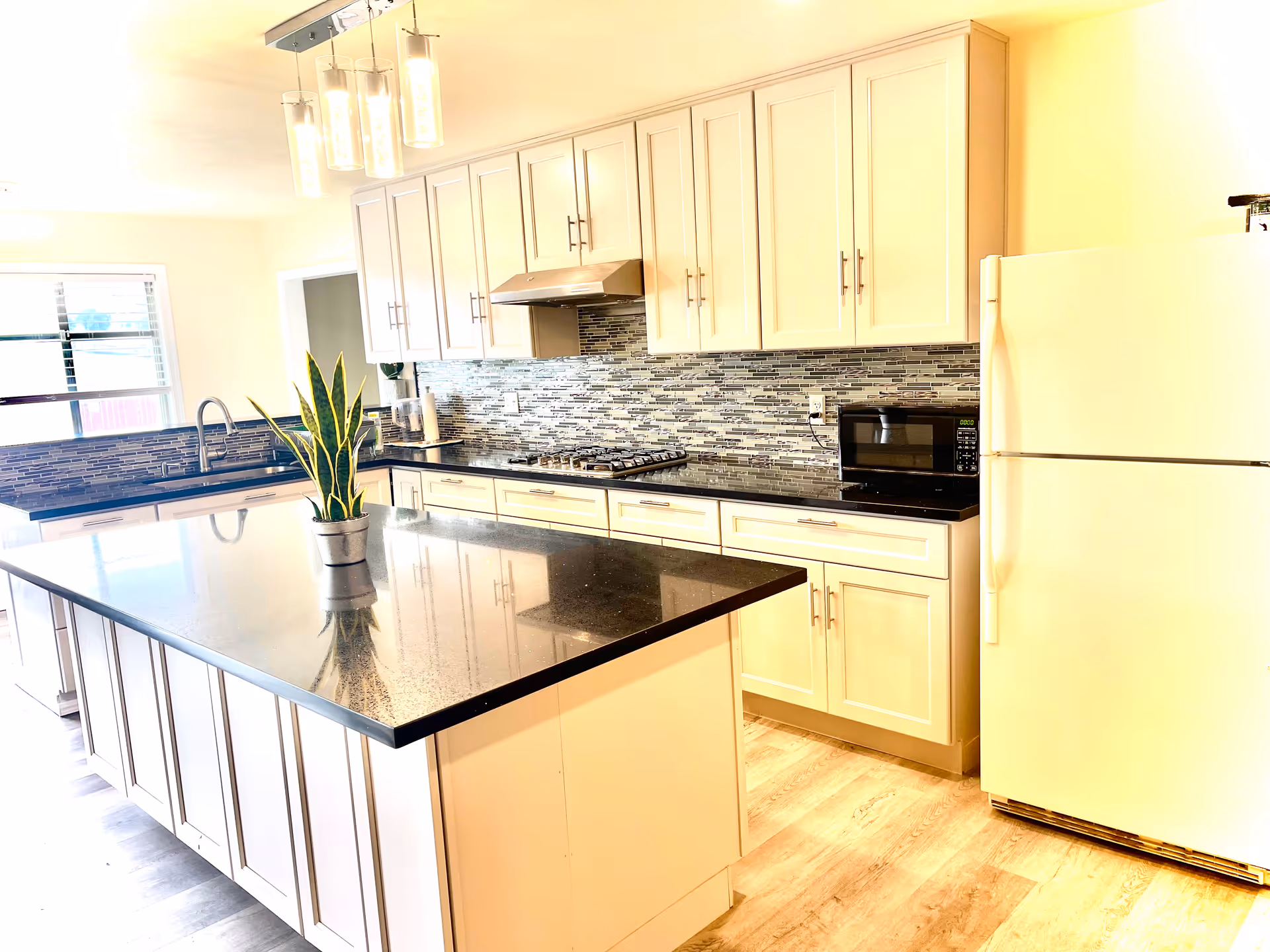 Bright modern kitchen with island, white cabinets, stainless appliances, and a potted plant.