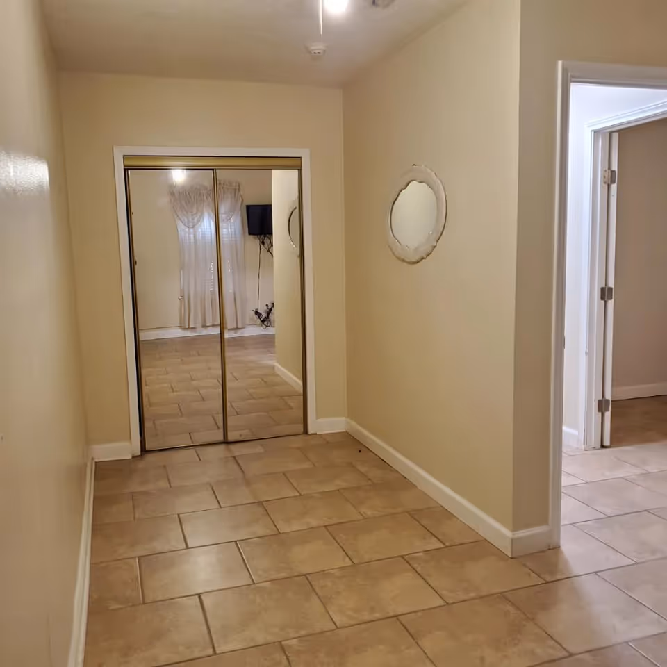 Tiled interior hallway with mirrored closet doors at the end and a round wall mirror on the right.
