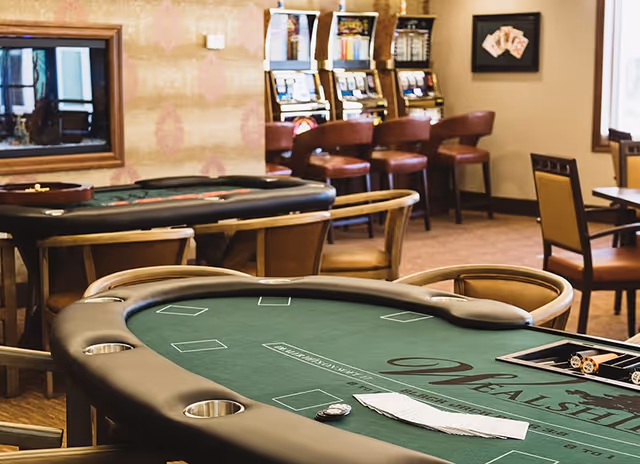 Interior gaming room with poker tables, chairs and slot machines.