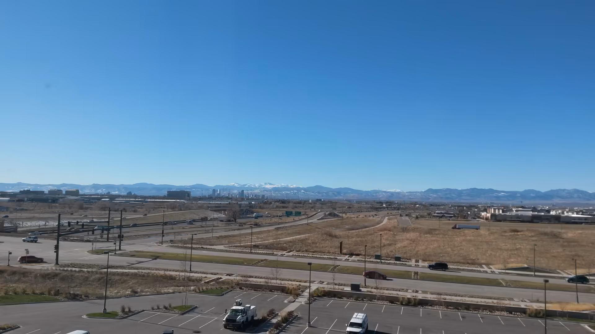 Sunny outdoor landscape showing roads, a parking lot, and distant mountains.