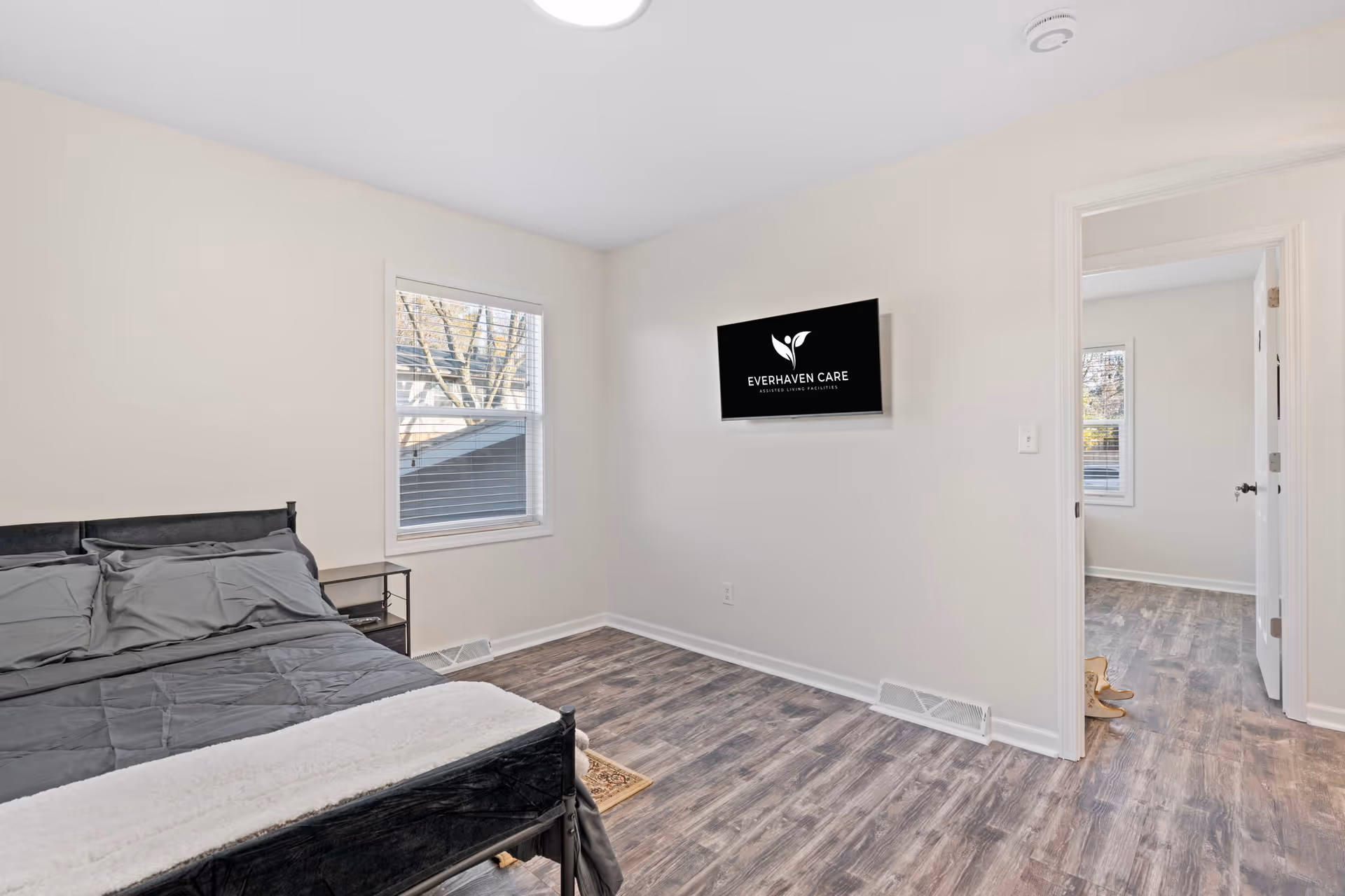 Bedroom with a bed, nightstand, window, and wall-mounted Everhaven Care TV.